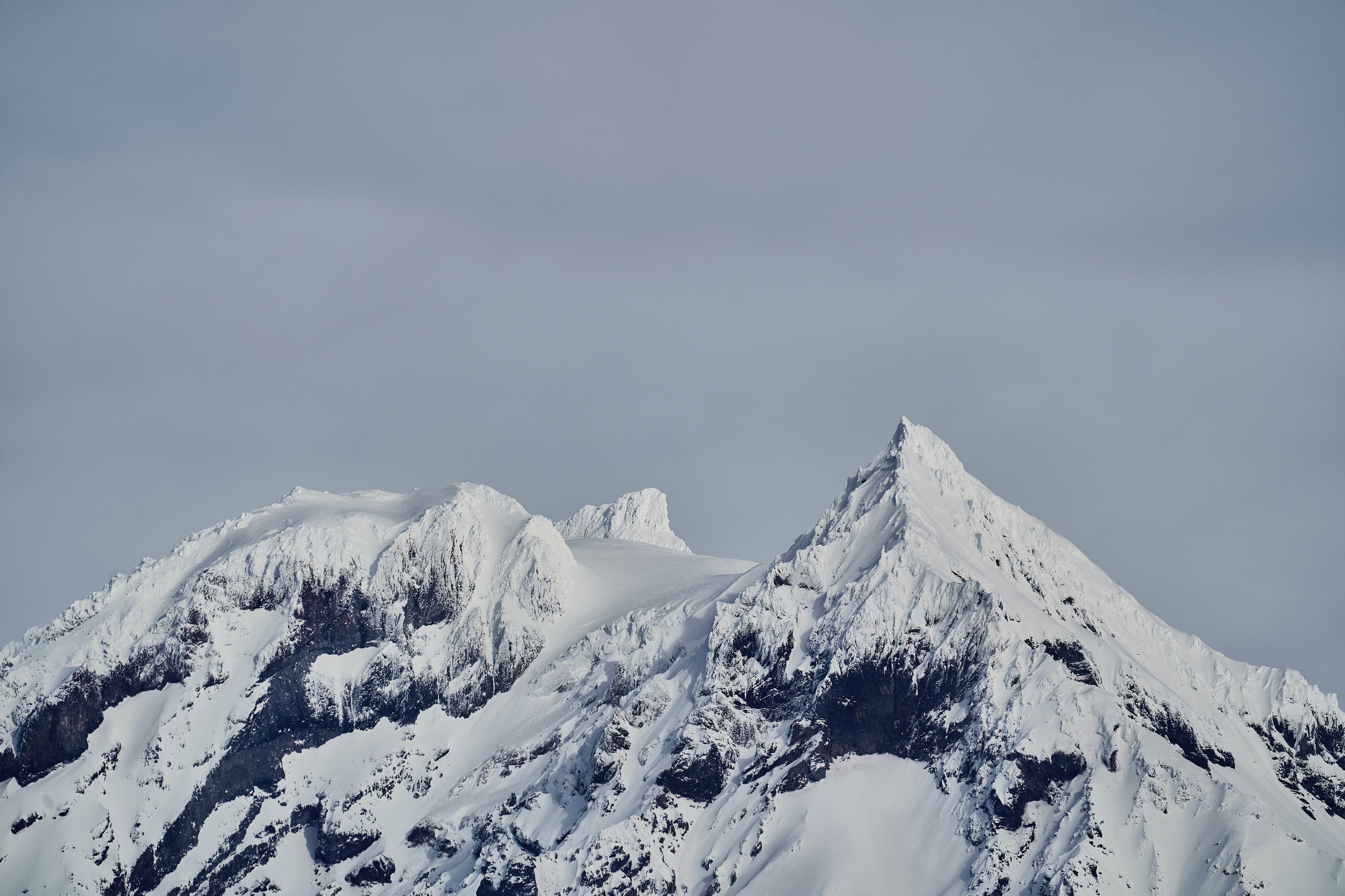 a_snowy_mountain_tops_with_a_grey_sky