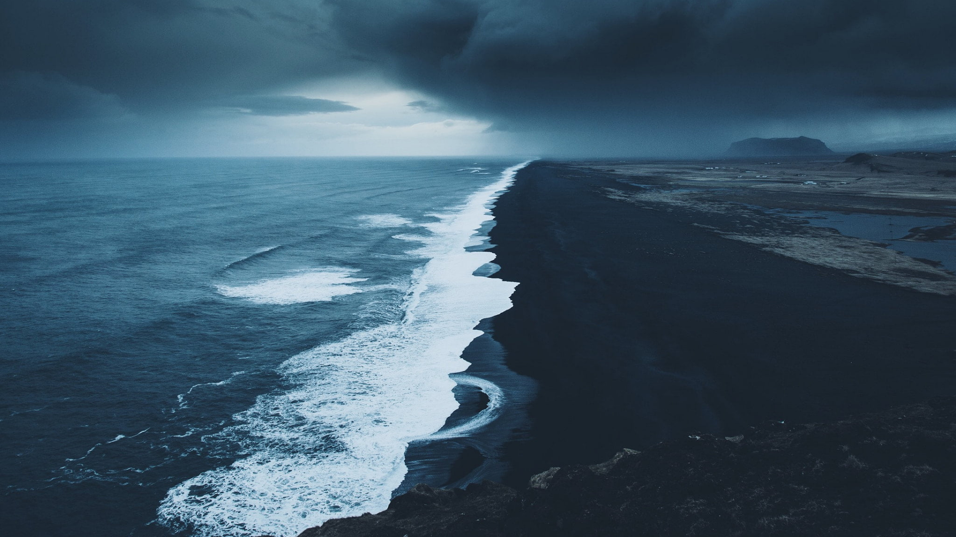 a_black_sand_beach_with_waves_and_clouds_above